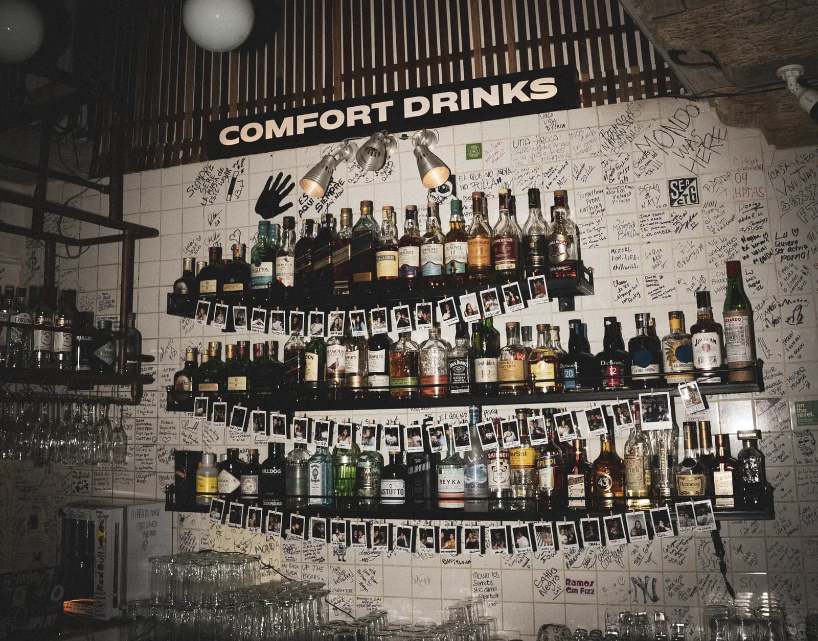 La pared de Barra 7: botellas, firmas a mano y el letrero Comfort Drinks