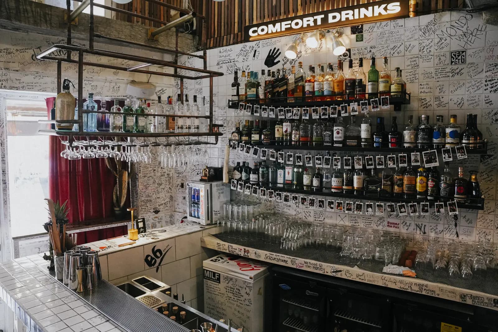 La barra de Barra 7: baldosa blanca, pared de botellas y el letrero Comfort Drinks
