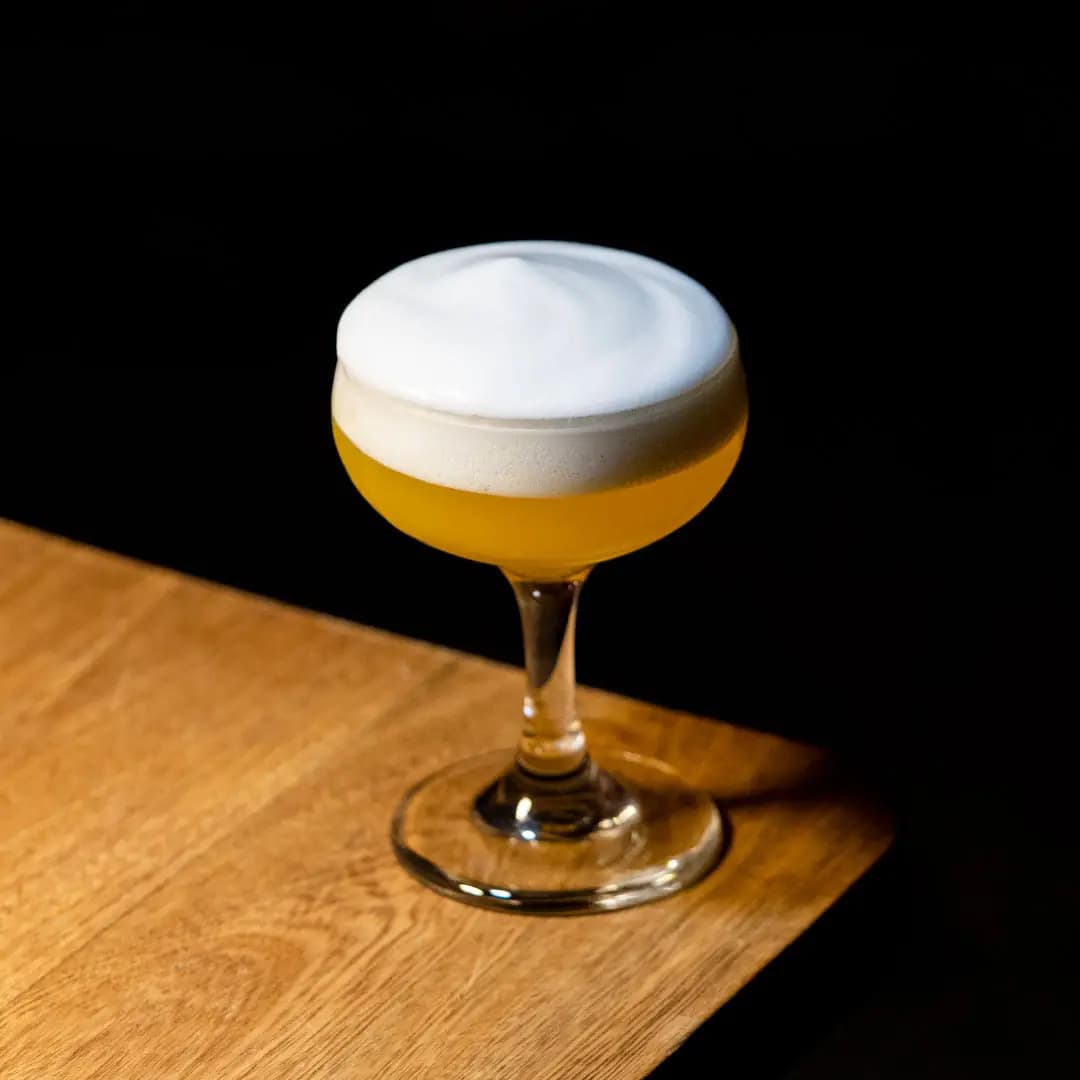 Cóctel con espuma servido en copa sobre la barra de madera